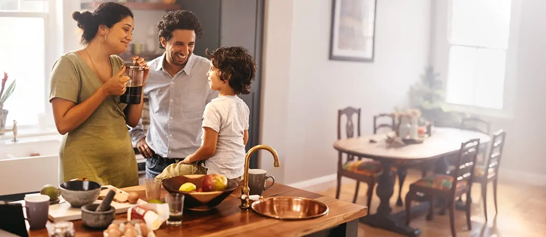 A family, mother, father, and son standing around a kitchen island as the mother holds a pot of French press coffee.