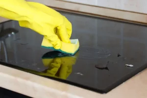 A yellow gloved hand holding a scrubby, cleaning a glass stovetop range.