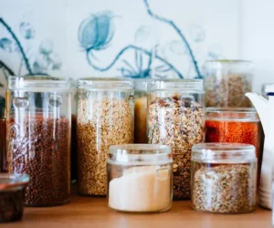 Several glass canisters of food on a kitchen counter holding various grains and ingredients.