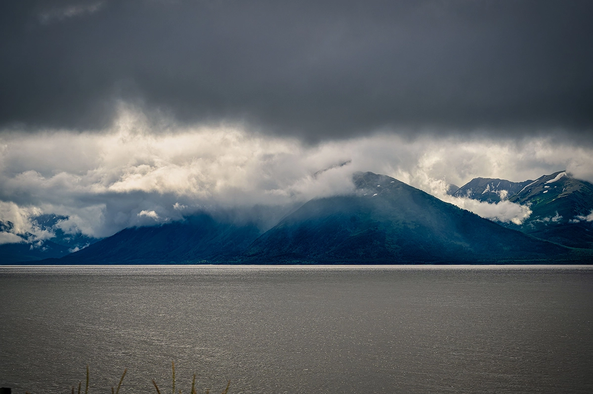 Fog-covered Alaskan mountains overlooking calm waters under a moody sky, representing Southeast Alaska’s natural environment.