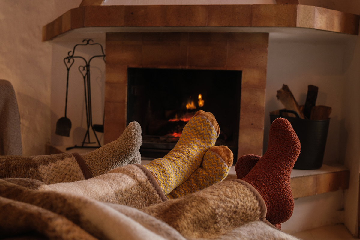 People wearing warm socks resting their feet near a lit wood burning fireplace, creating a cozy winter indoor scene.