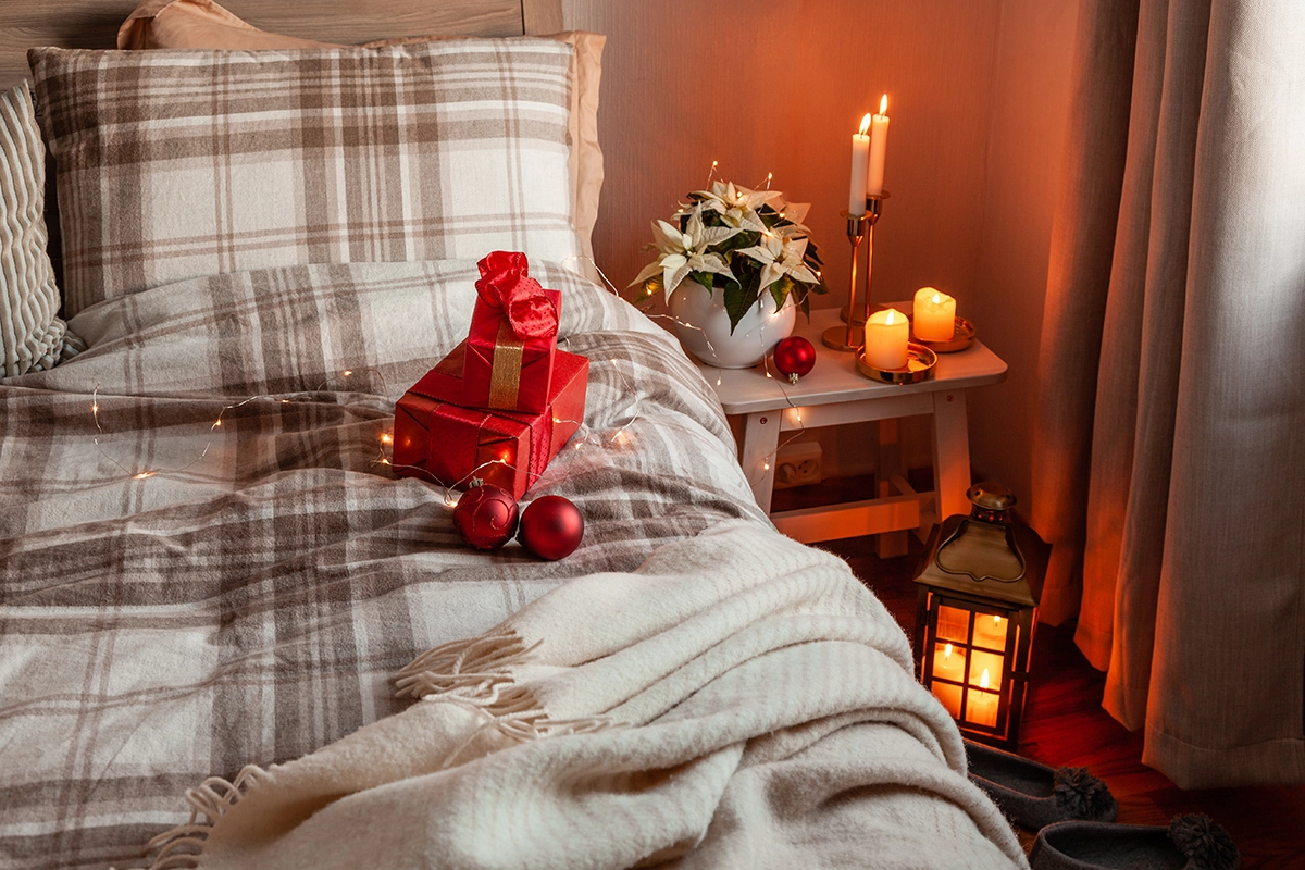 Warm bedroom decorated for the holidays with candles, wrapped gifts, ornaments, and soft lighting.
