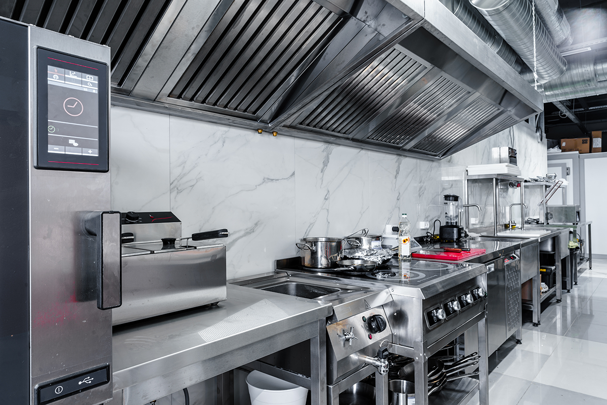 Clean stainless steel commercial kitchen with industrial stove, fryer, and ventilation hood