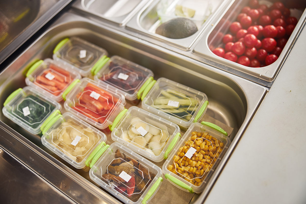 Prepped ingredients stored in sealed containers inside stainless steel deli prep station