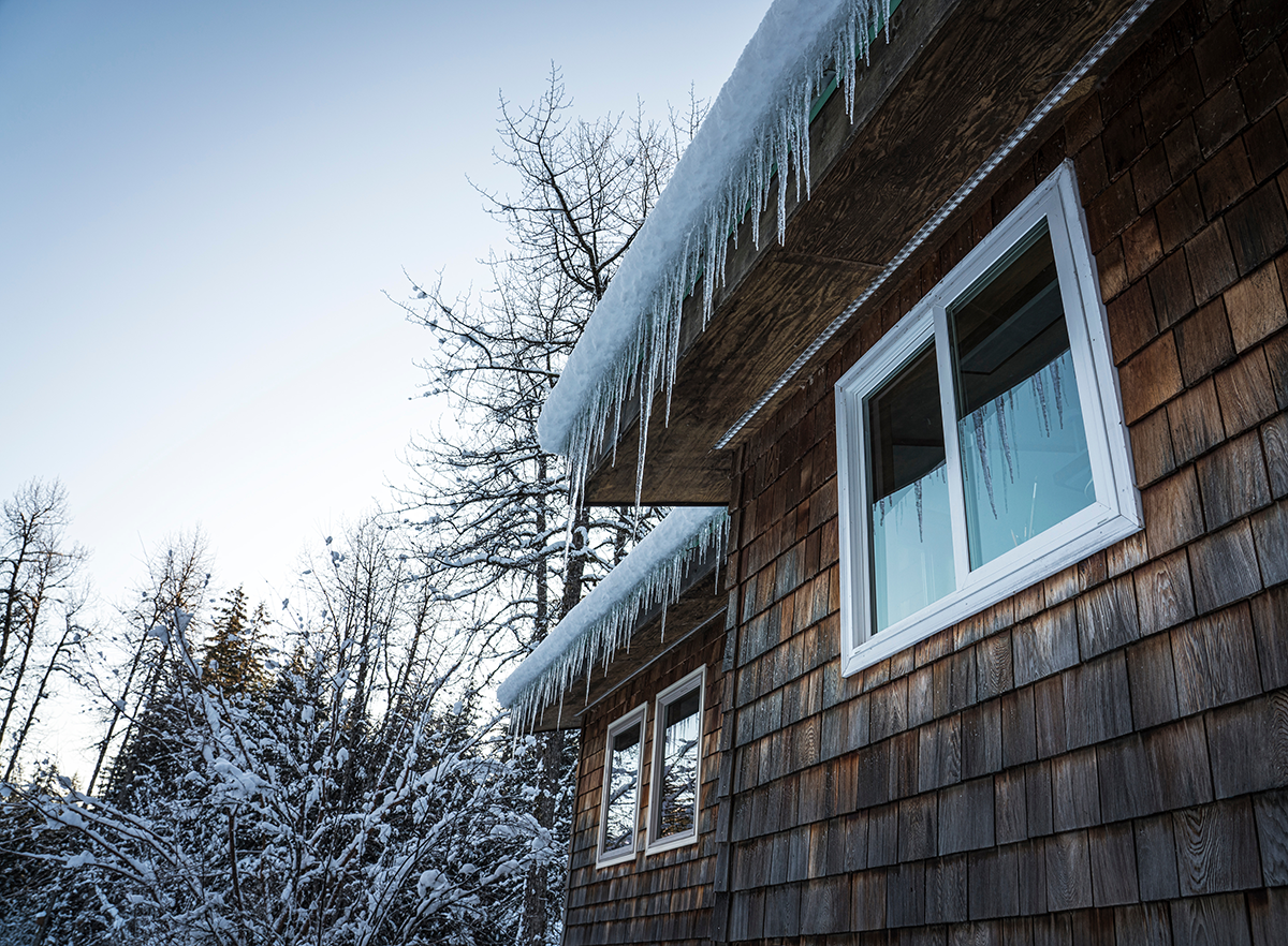 House exterior in winter with snow and icicles along the roofline, showing cold weather conditions that drive pests indoors.
