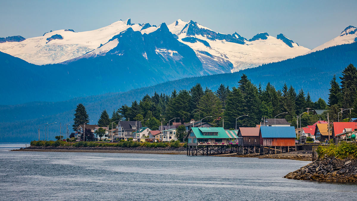 Coastal town of Petersburg, Alaska with colorful waterfront buildings, forested shoreline, and snow capped mountains in the background.