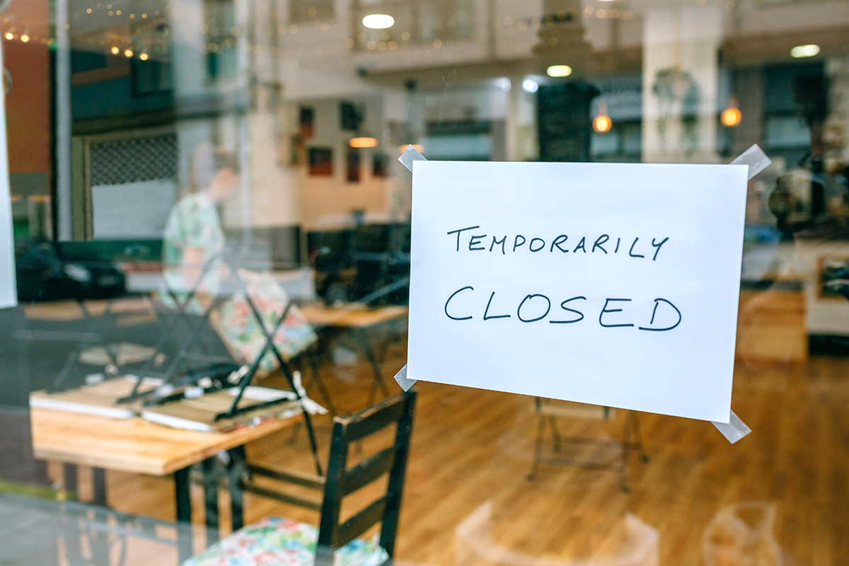 Temporarily closed notice taped to a restaurant glass door with empty dining area visible inside
