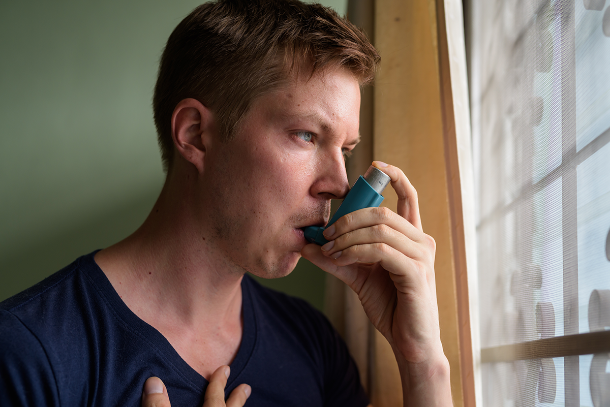 Young man using an asthma inhaler indoors, highlighting respiratory health concerns inside the home.