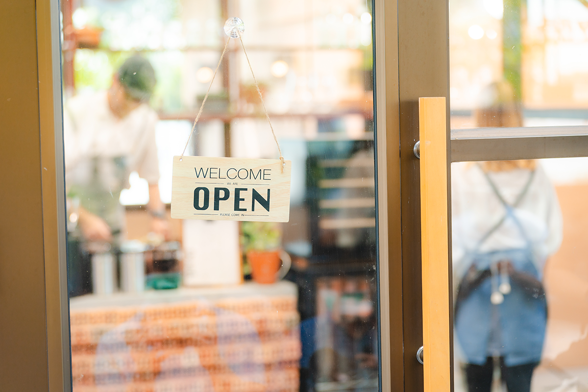 Coffee shop glass door with welcome open sign and blurred barista inside café