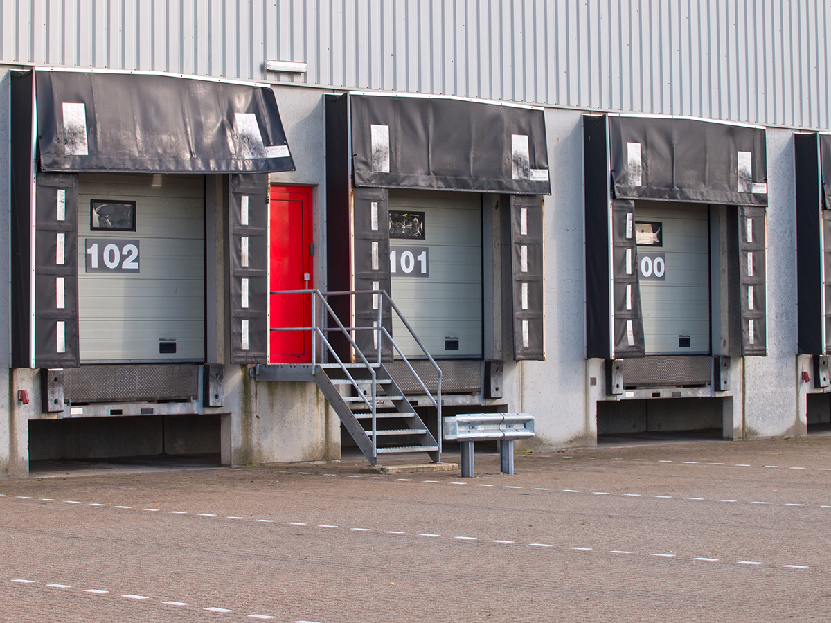 Industrial loading dock doors with numbered bays and red service door at distribution center