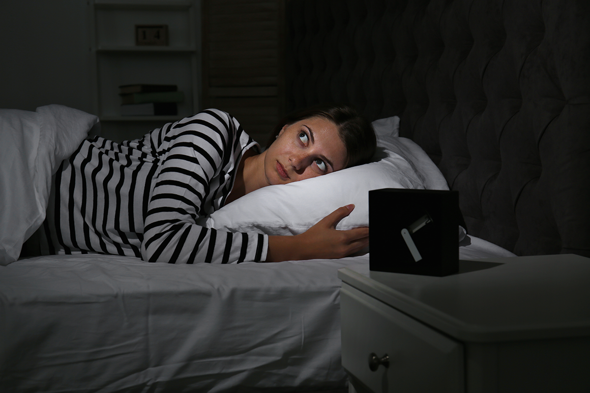 Woman lying awake in bed at night looking worried beside an alarm clock in a dark bedroom