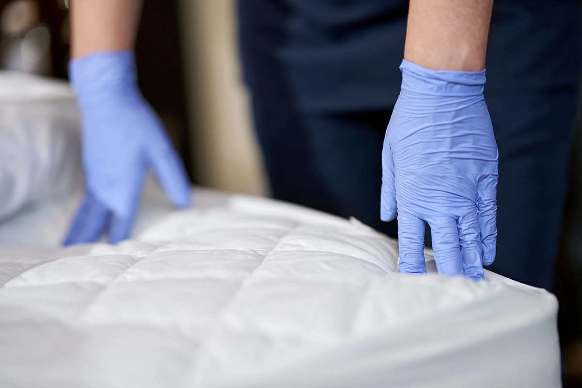 Gloved hands inspecting a mattress for signs of bed bugs during a professional pest inspection