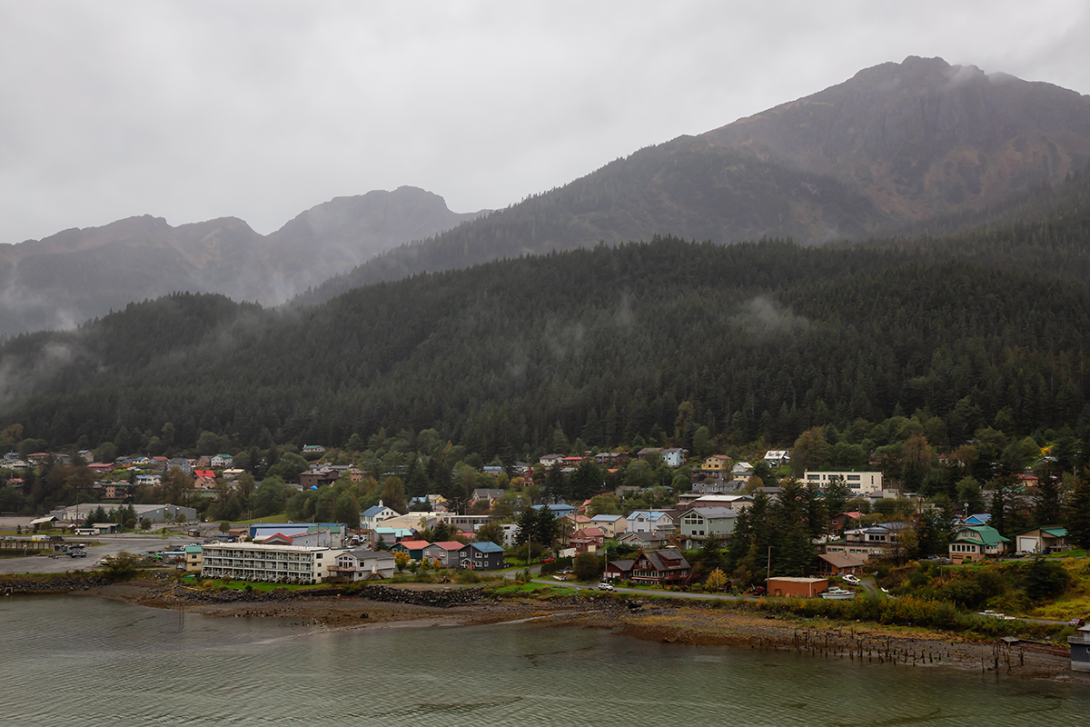 Cloudy coastal view of Juneau, Alaska, with mountains, forest, water, and buildings along the shoreline.