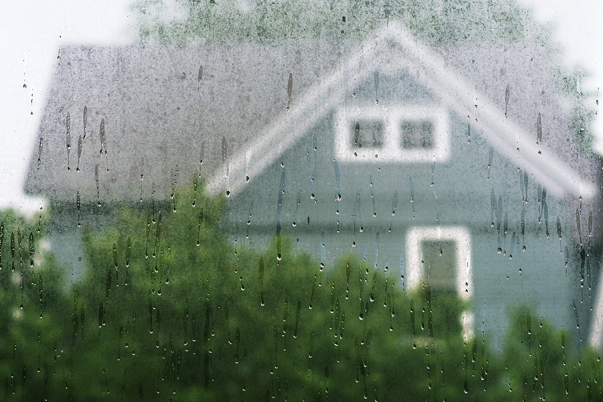 Blue house seen through a rain-covered window, showing moisture buildup, condensation, and water droplets on glass.